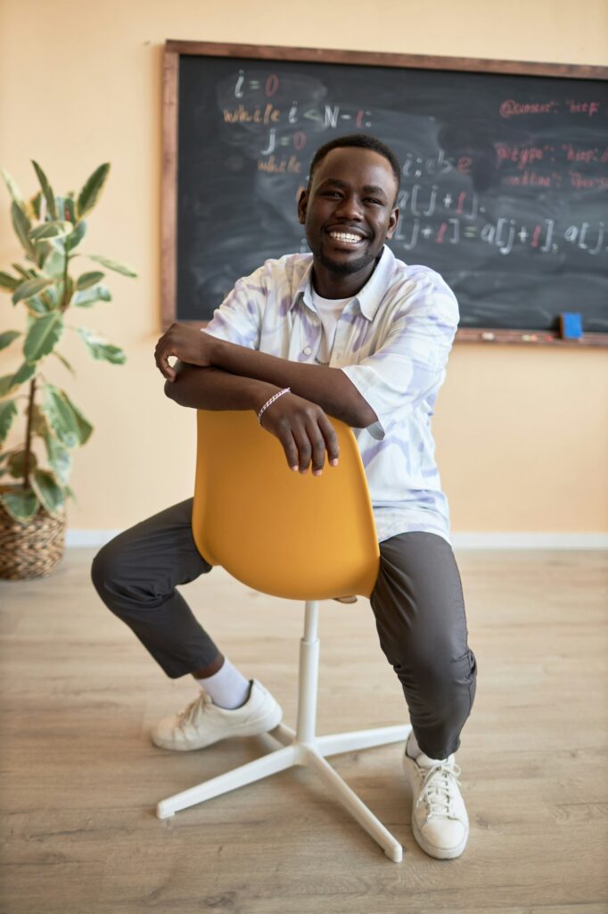 Young cheerful African American male student sitting on chair in classroom